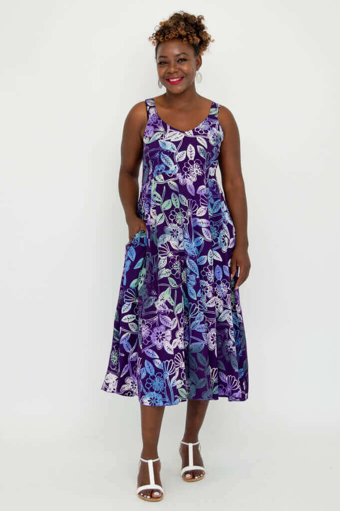Woman standing with hand in pocket, wearing a purple floral sleeveless dress