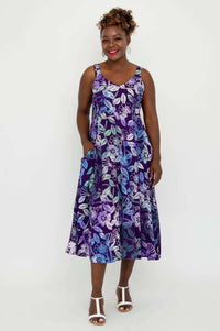 Woman standing with hand in pocket, wearing a purple floral sleeveless dress
