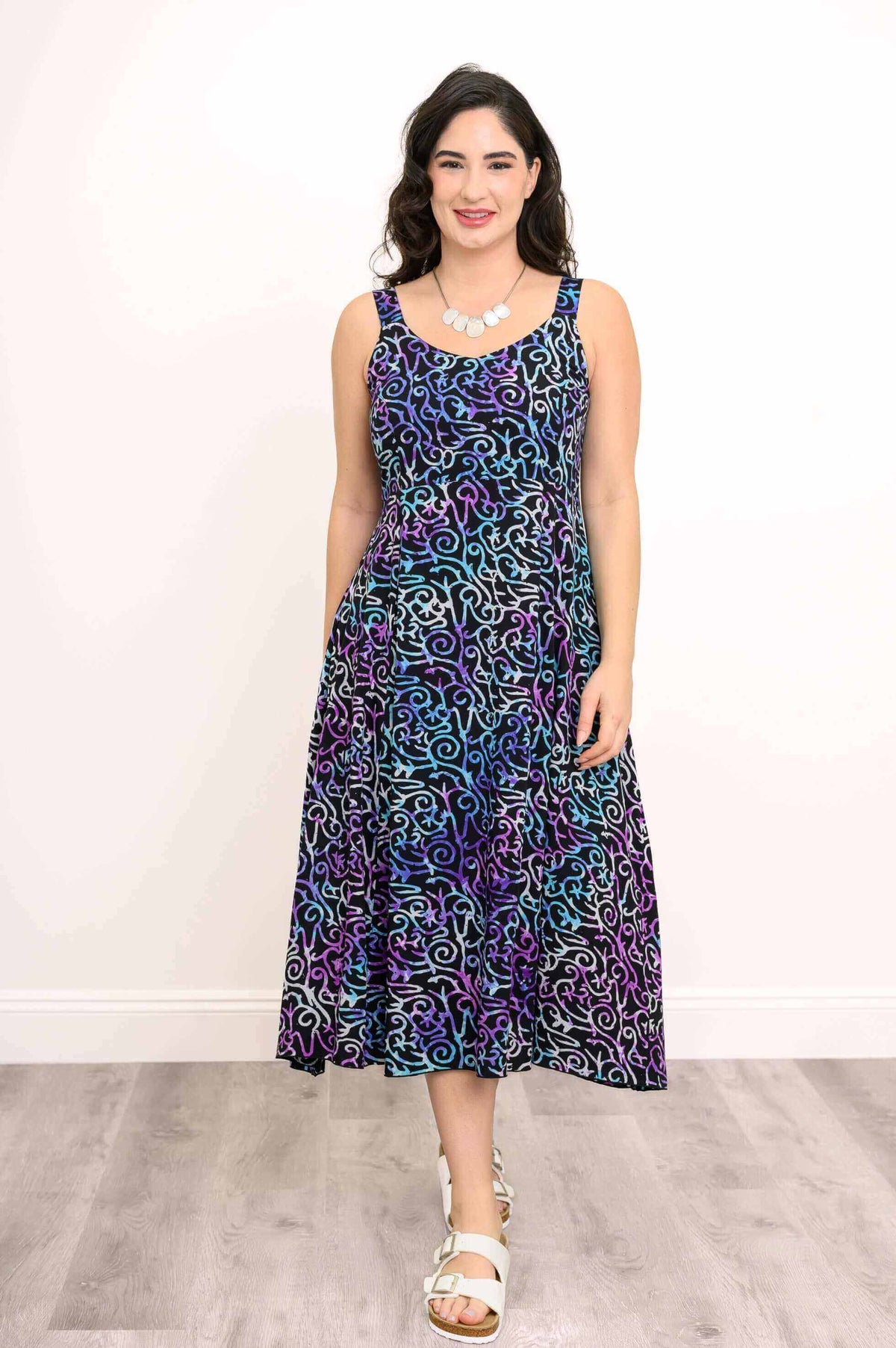 Model wearing a sleeveless A-line midi dress with blue, purple, and black swirling pattern, front view