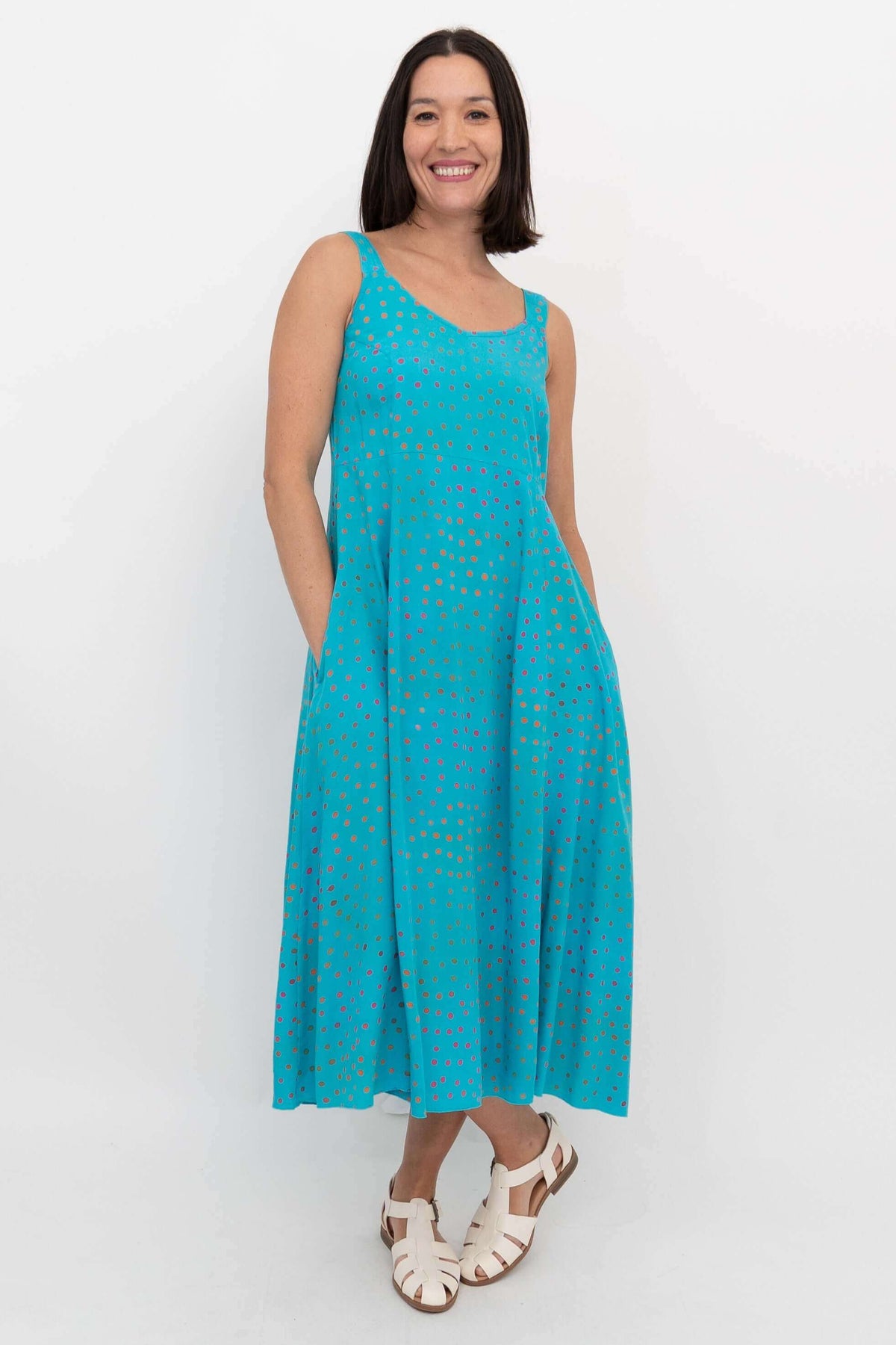 Woman in a turquoise dotted dress with hands in pockets, angled front view