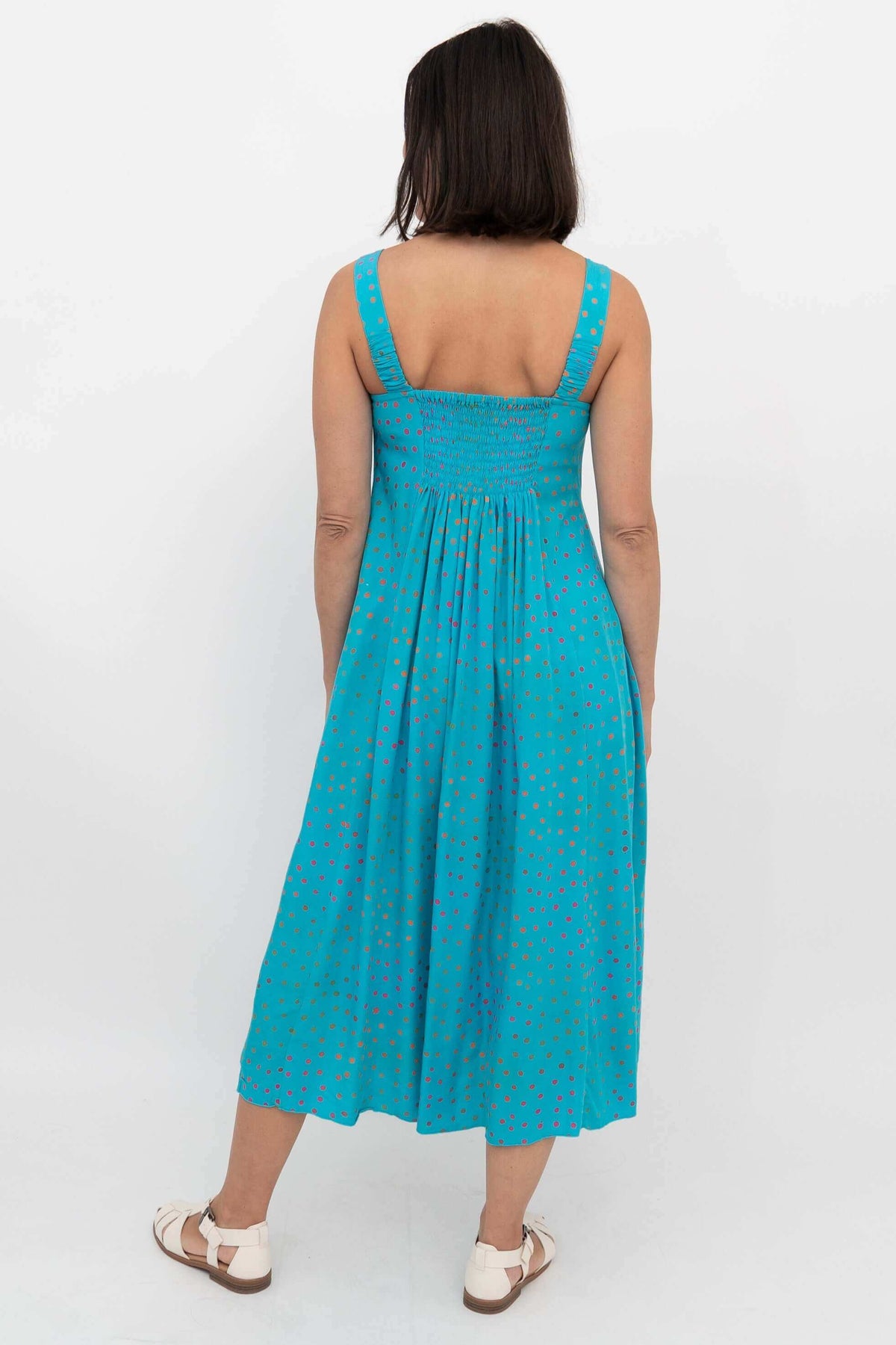 Back view of a woman in a turquoise sleeveless dress with shirred bodice