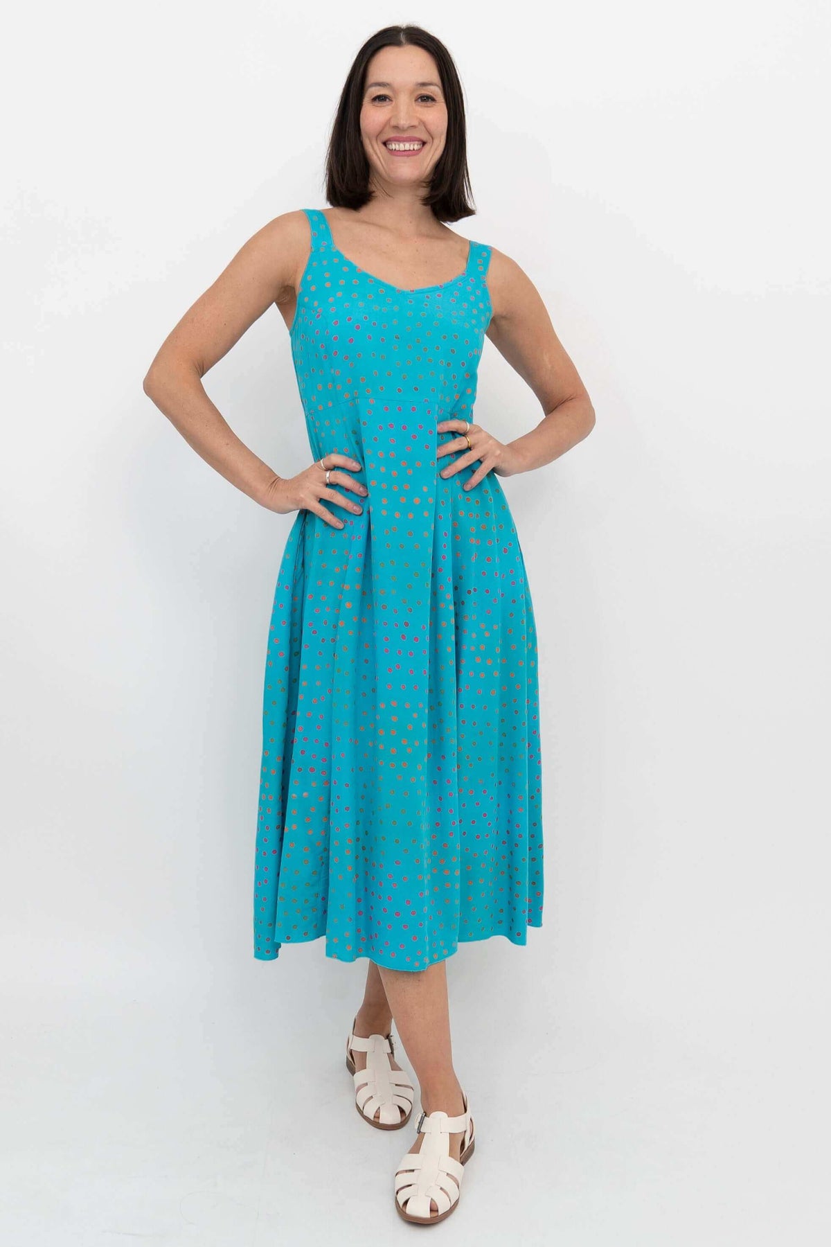 Woman wearing a turquoise sleeveless A-line dress with colorful dots, front view