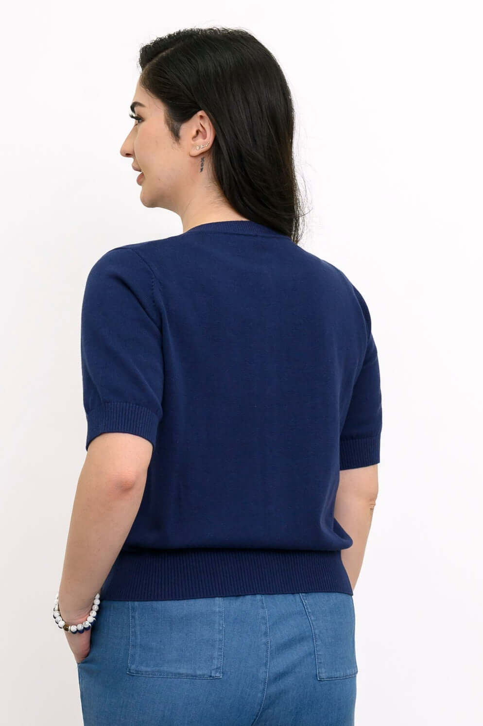 Back view of woman wearing the indigo Shen short sleeve cardigan, showing ribbed hem