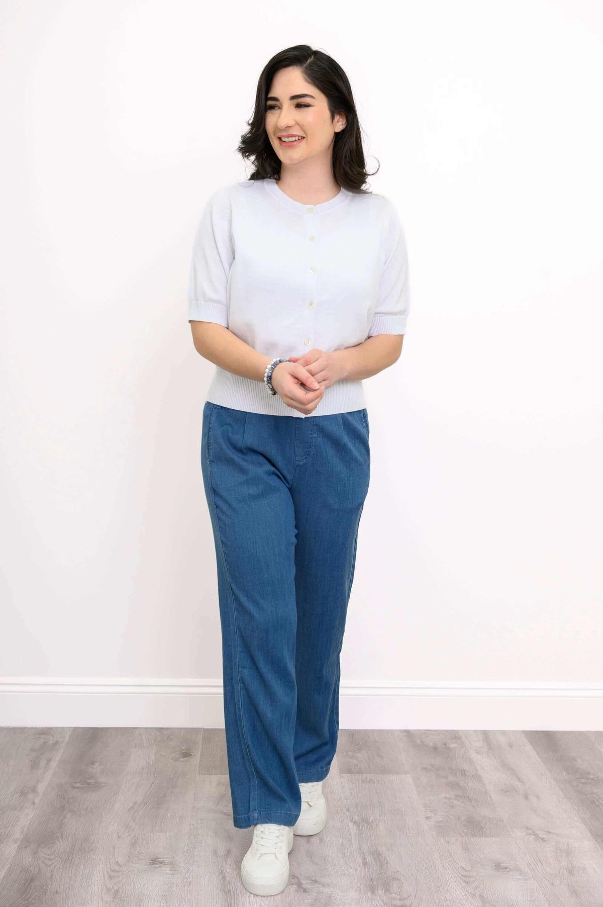 Model smiling in a short-sleeve white cardigan and blue pants