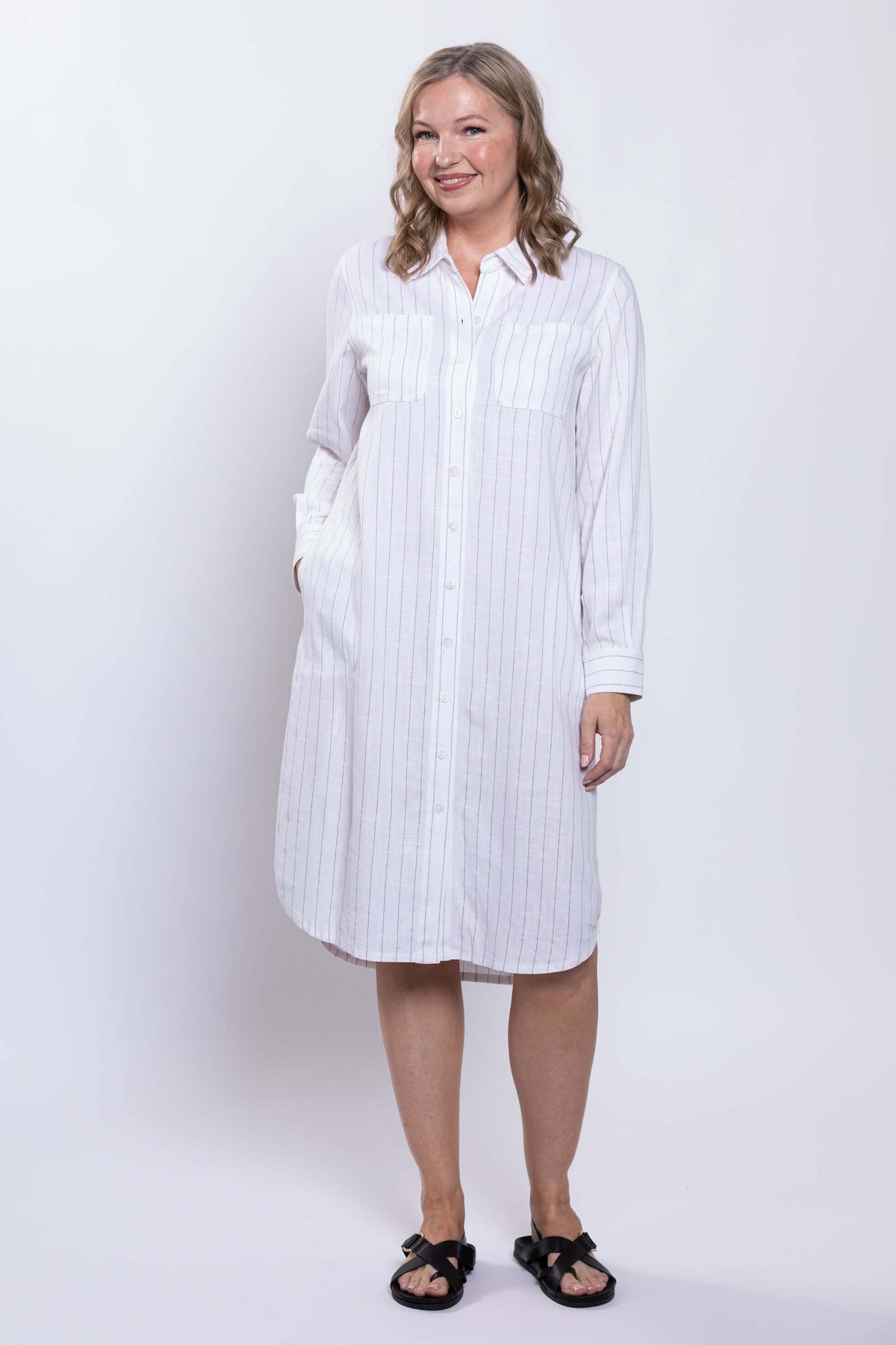 Side-angled view of a woman in a white striped shirt dress with pockets