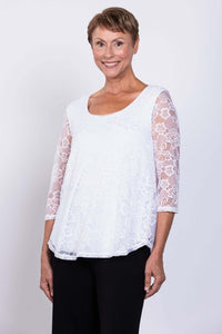 Side-front view of a woman smiling in a white lace overlay 3/4 sleeve top and black pants