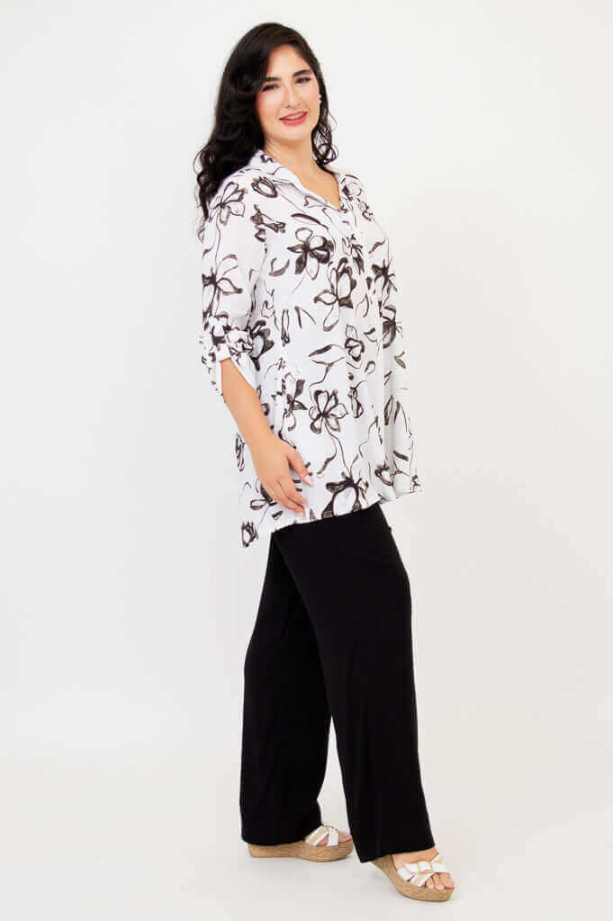 Woman in white floral tunic paired with black pants, angled side view
