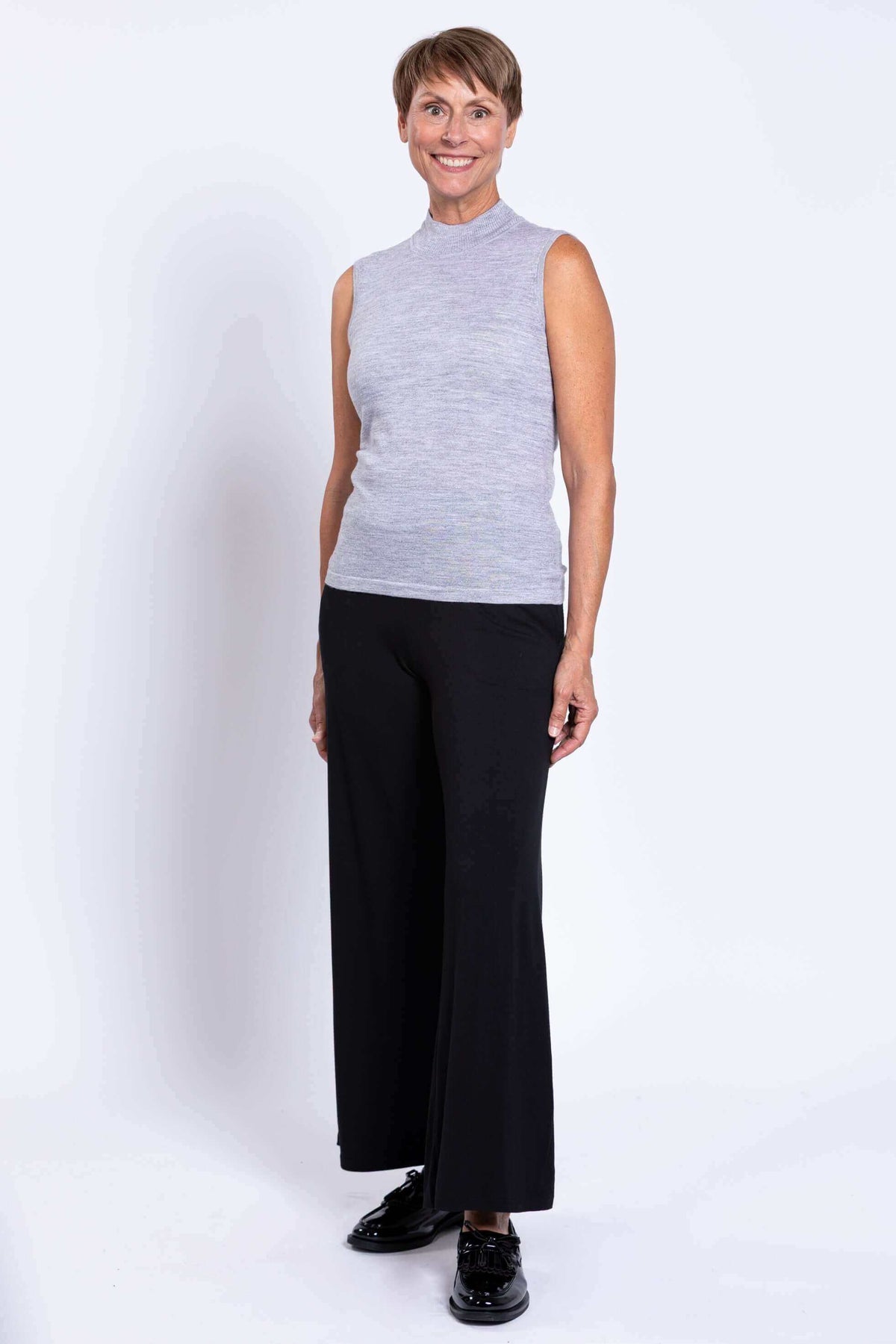 Side view of woman in grey sleeveless mock neck sweater with black pants