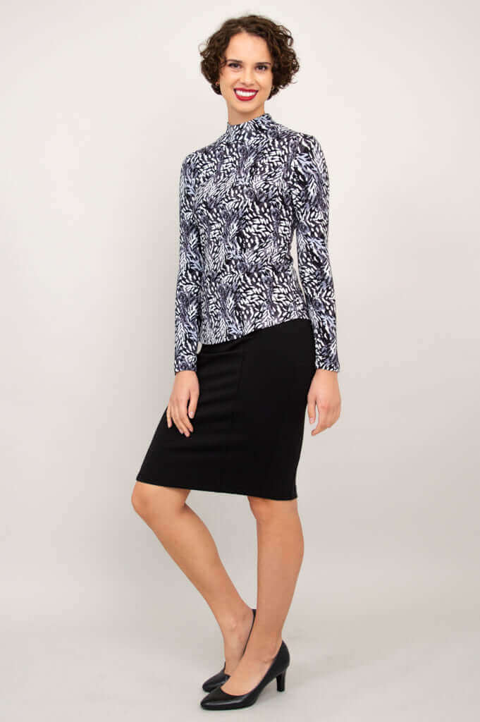 Side-angled view of a woman modeling a black and white palm print mock neck top and black skirt