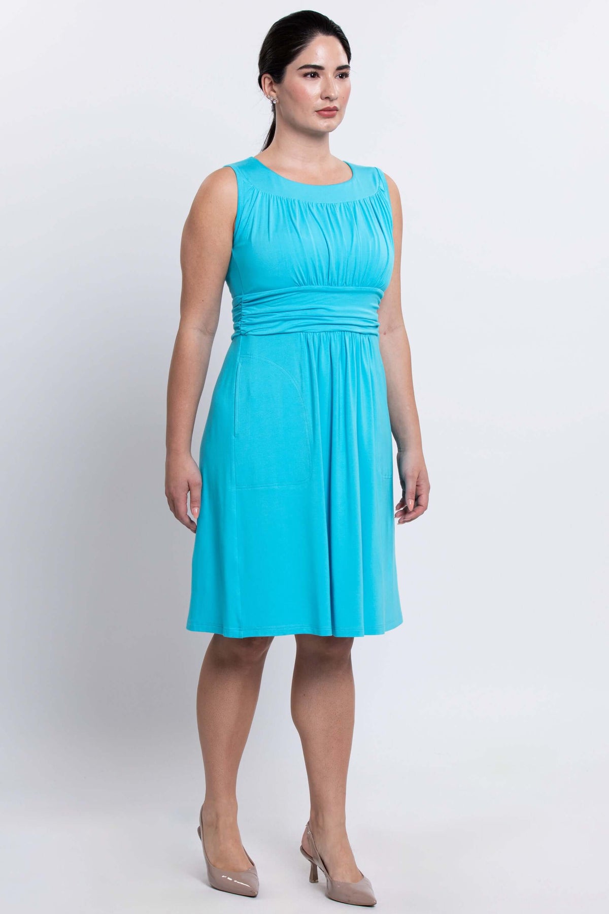 Angled side view of woman in aqua blue ruched bodice knee-length dress