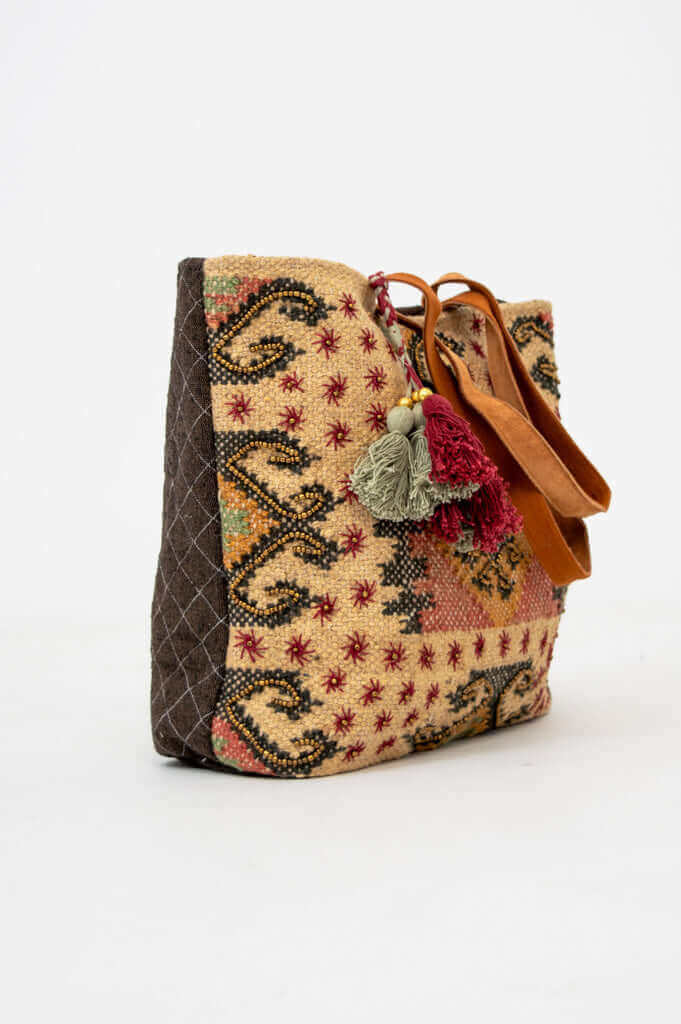 Side angle showing the tote bag's detailed pattern and decorative tassels