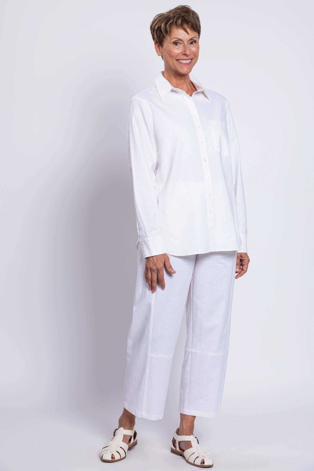 Side angled view of a woman smiling in a white button-up shirt and white pants