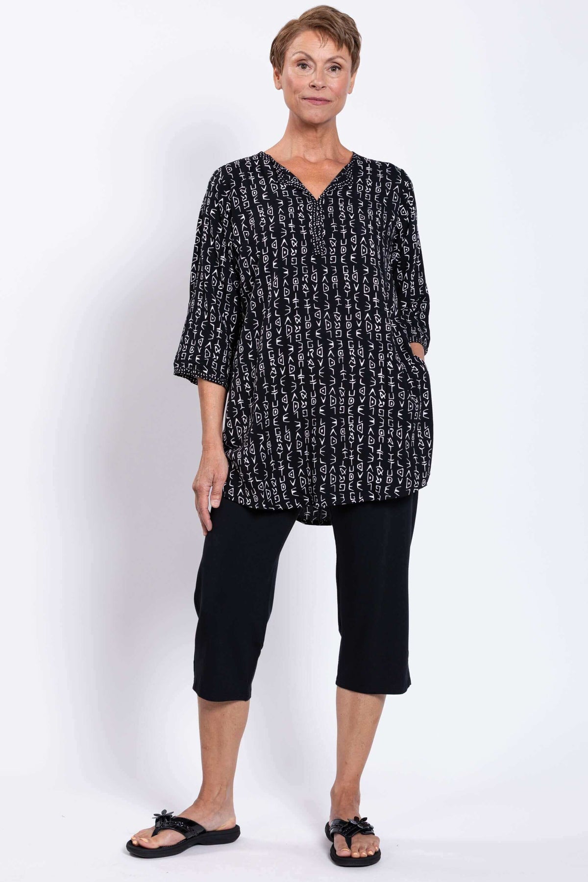 Three-quarter view of a woman in a black tunic with side pockets and white pattern