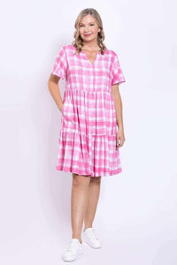 Woman with hand in pocket, wearing pink check tiered dress with short sleeves and V notch neckline