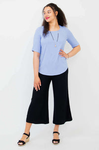 Model posing to the side in light blue blouse and black pants