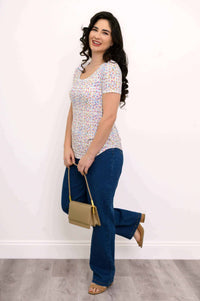 Woman in a confetti dot Tessa Tee, blue jeans, holding a tan bag, playful side pose
