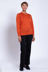 Woman in side-facing pose wearing a tangerine merino wool V-neck sweater.