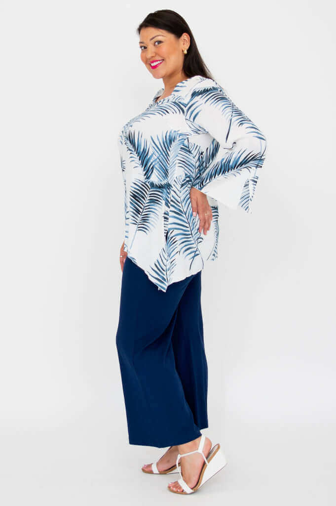 Side view of woman in white and blue palm print top with navy pants