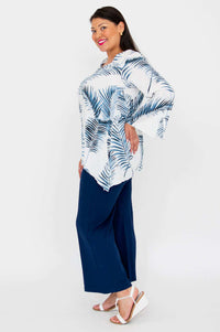 Side view of woman in white and blue palm print top with navy pants