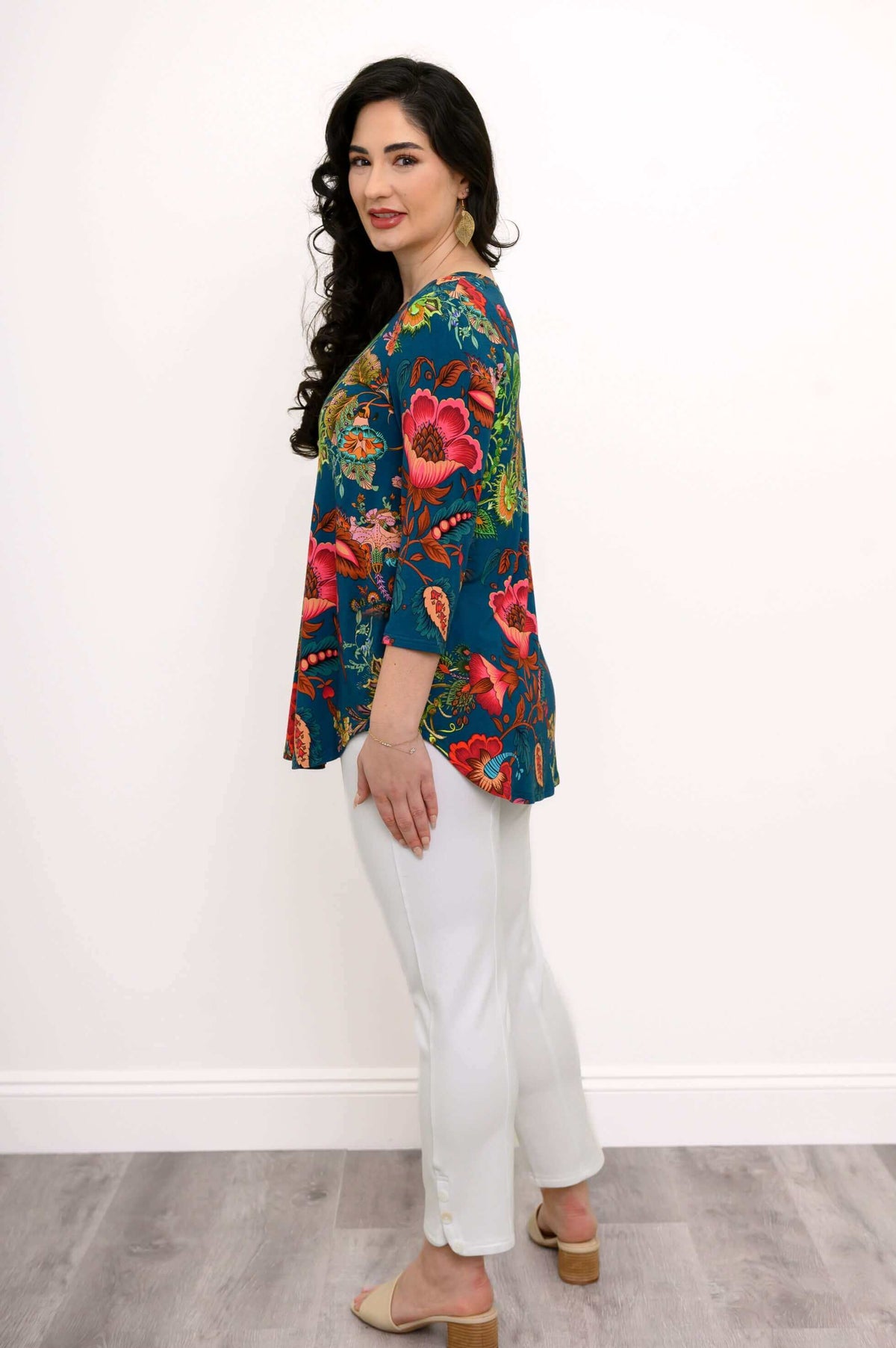 Side profile of woman in 3/4 sleeve top with rounded hem and floral print, with white pants
