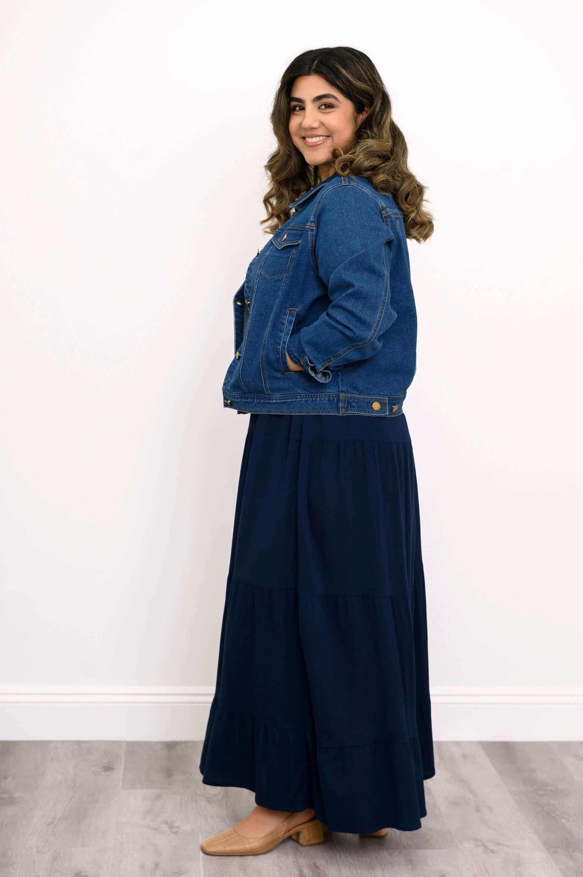 Model in navy tiered maxi skirt and denim jacket, side profile with hands in pockets