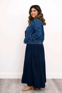 Model in navy tiered maxi skirt and denim jacket, side profile with hands in pockets