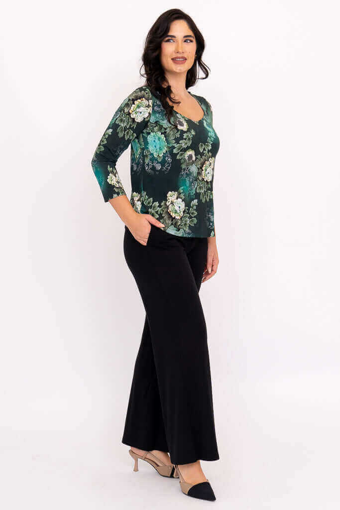 Side view of model in green floral top and black pants with hand in pocket