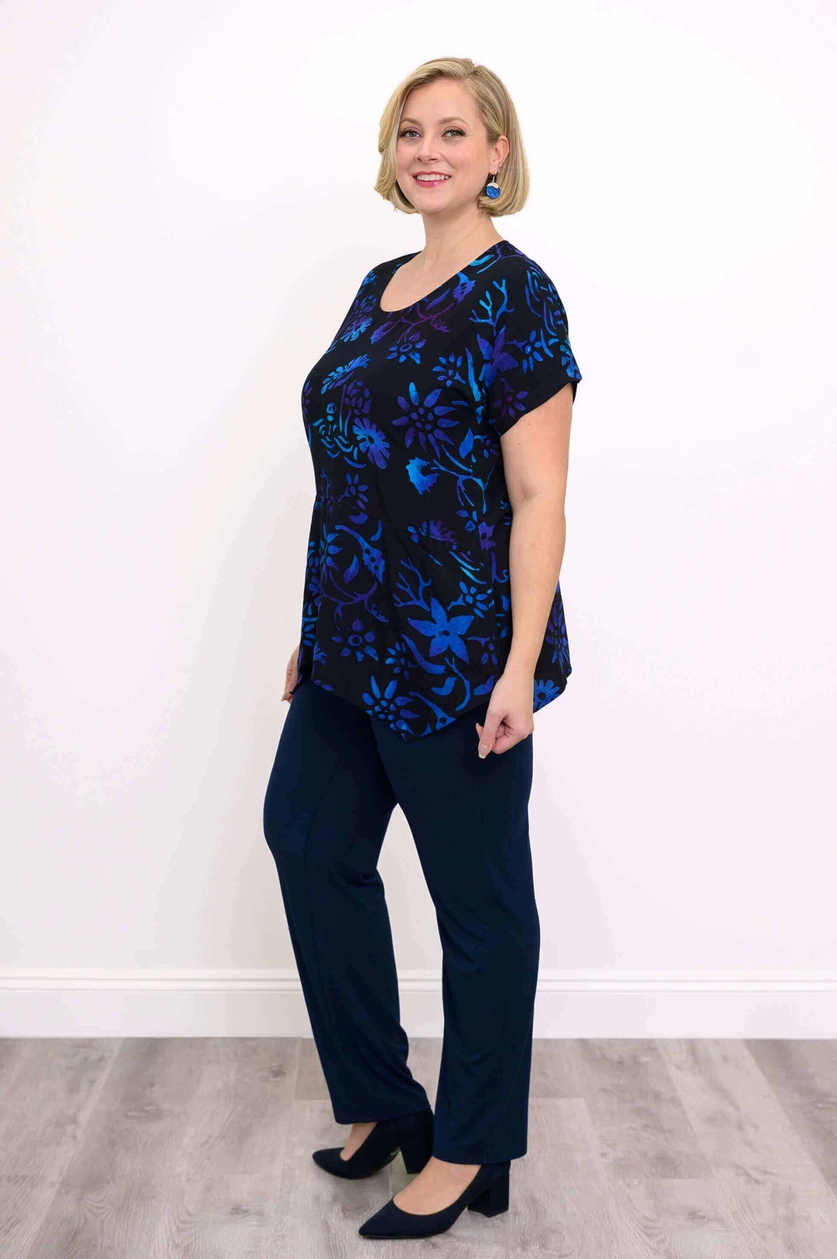 Side view of plus size model in blue and purple floral curved-hem tunic and navy pants