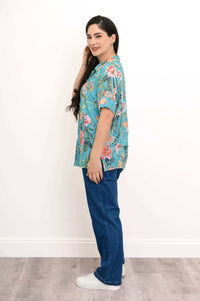 Side view of a woman wearing a vibrant turquoise floral blouse and blue jeans