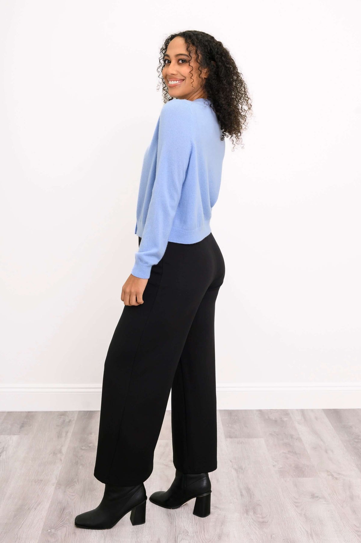Side view of a woman in a light blue cashmere cardigan and black pants, smiling