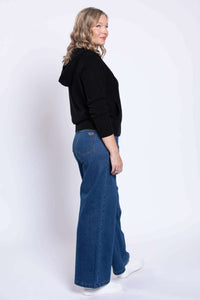 Side view of woman in wide leg blue jeans, black zip hoodie, and white sneakers