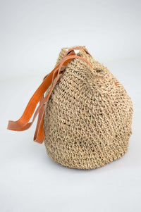 Side profile of a woven rattan bag with tan leather straps