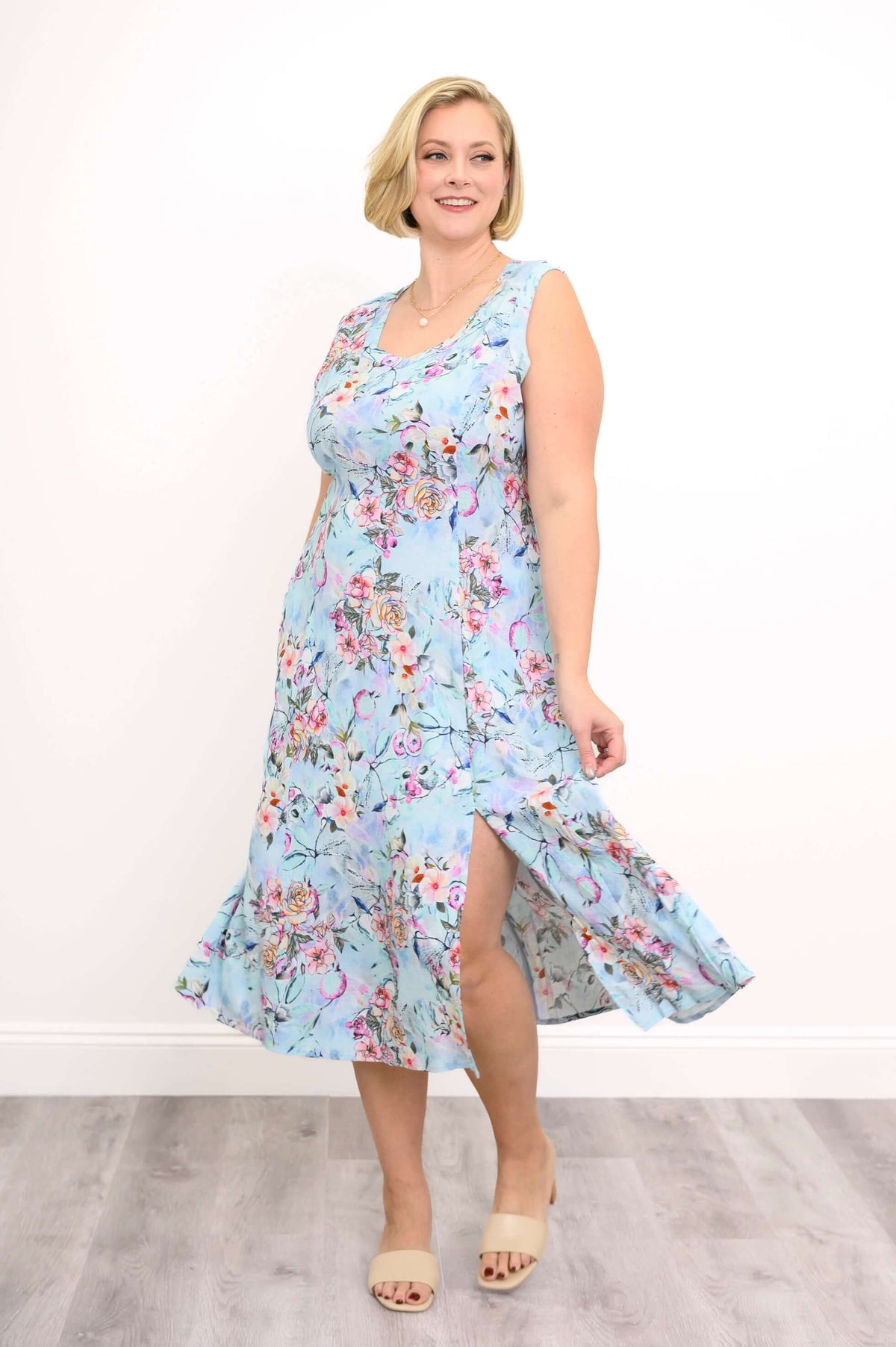 Woman showing side slit detail on a sleeveless blue floral midi dress