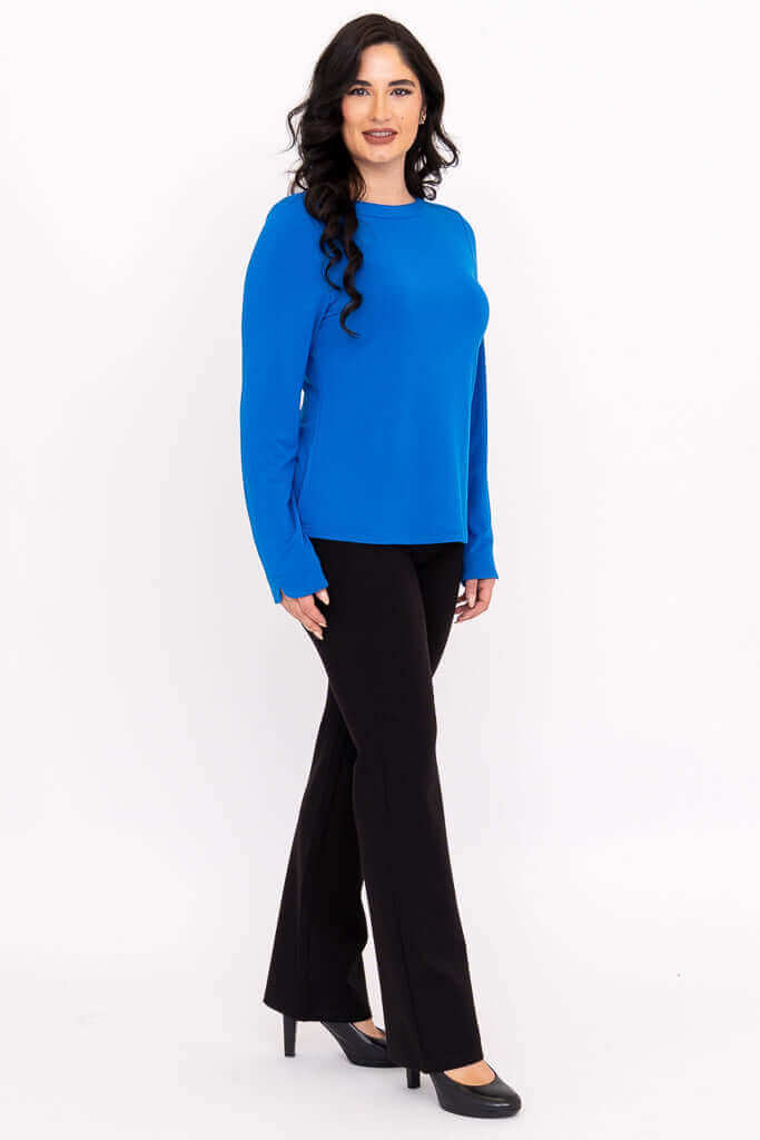 Side view of woman modeling blue boat neck top with black pants and heels