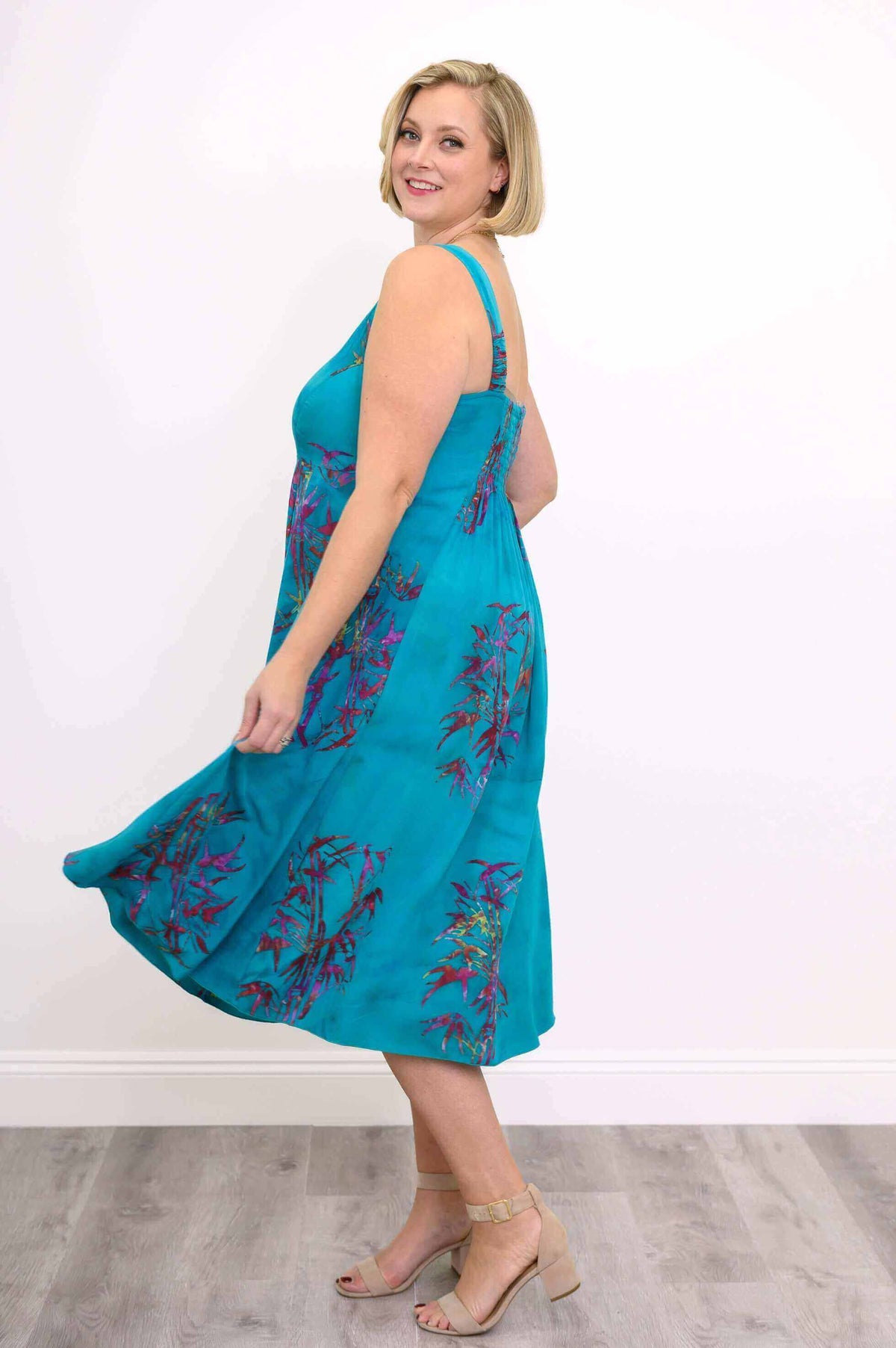 Side view of woman twirling in an aqua blue floral sleeveless midi dress