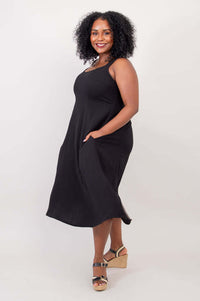 Side view of model showing the pockets and flowy skirt of the black midi dress