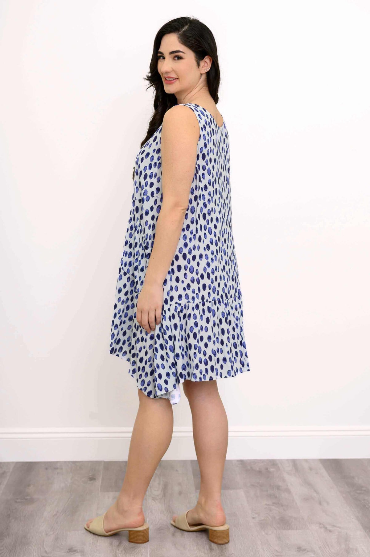 Side view of model in a sleeveless blue and white print dress with flowy hem