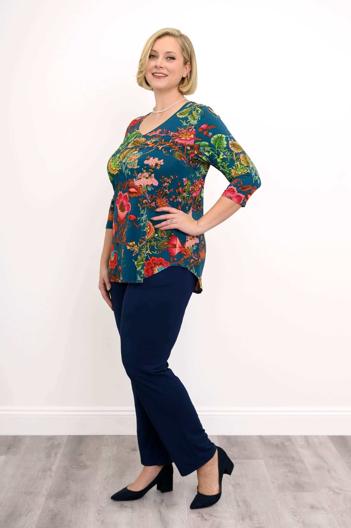 Full body angled view of woman wearing bright floral patterned top and navy pants