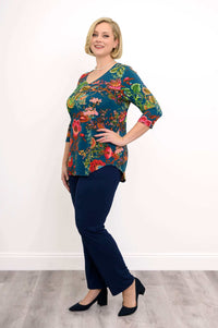 Full body angled view of woman wearing bright floral patterned top and navy pants