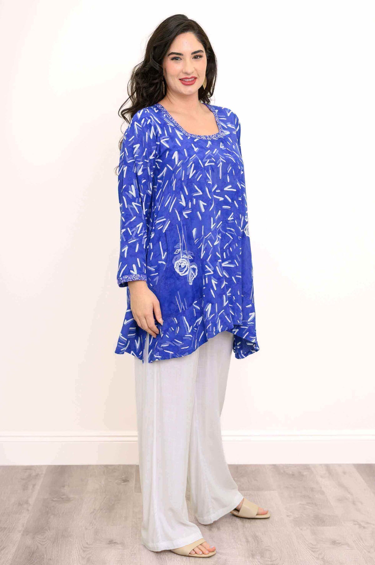 Side view of woman in blue patterned shark-bite tunic and white pants