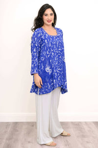 Side view of woman in blue Maria tunic with white print, paired with light trousers