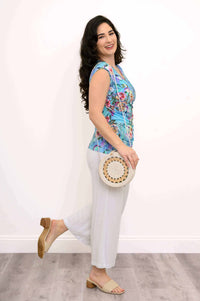 Woman posing side view in floral tank top with white pants and woven bag