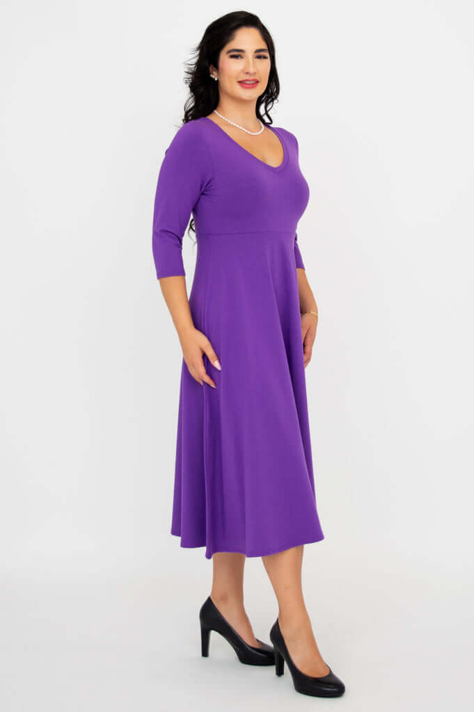 Side view of a woman in a purple midi dress with three-quarter sleeves and black heels