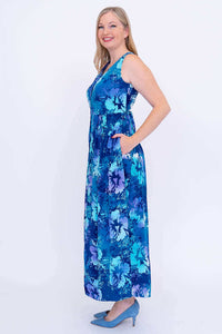 Side view of a woman modeling a blue floral sleeveless maxi dress with pockets