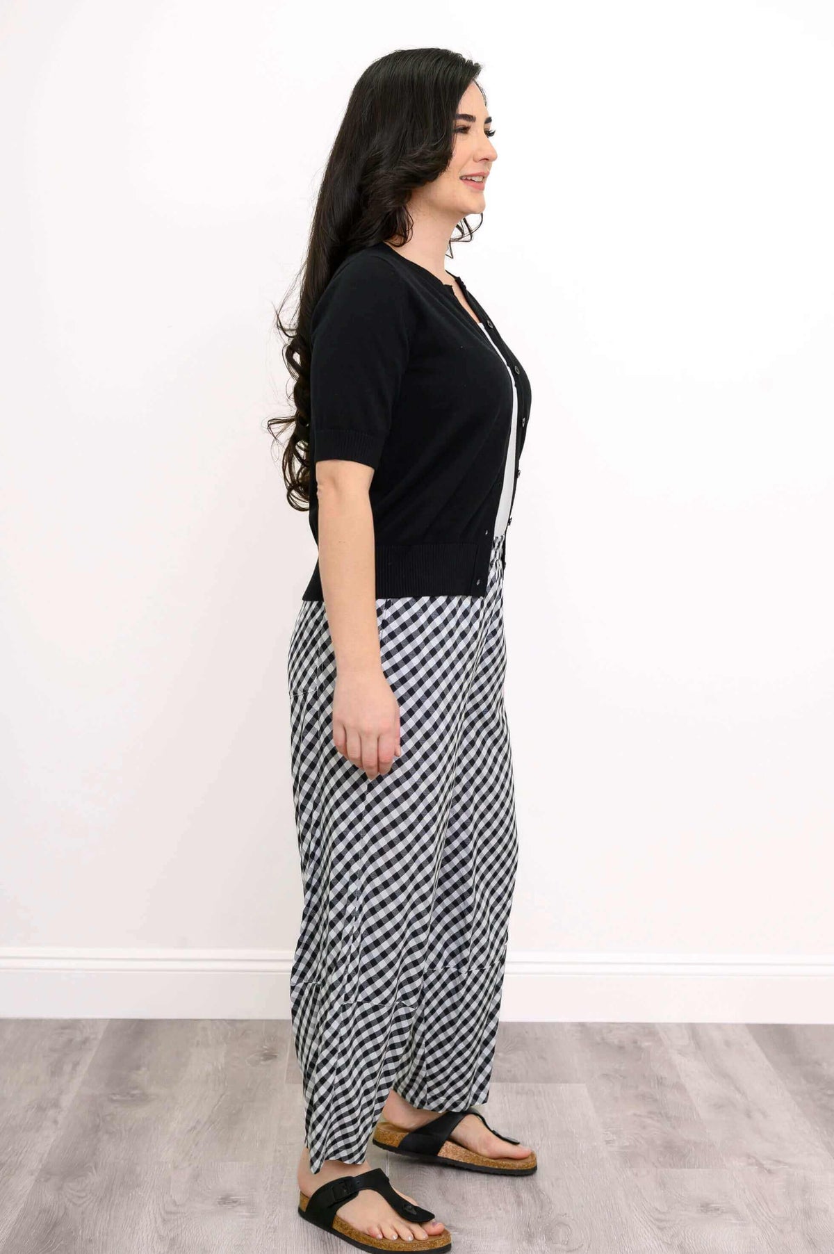 Side view of black and white gingham pants styled with a black cardigan and sandals