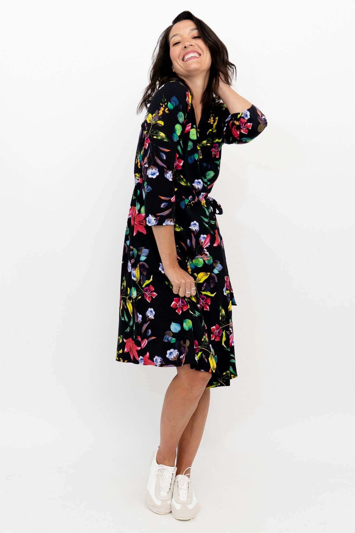 Side view of woman smiling in a black floral tie-waist wrap dress