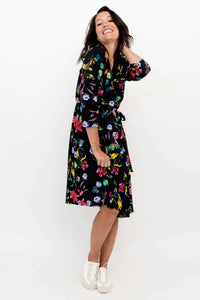 Side view of woman smiling in a black floral tie-waist wrap dress