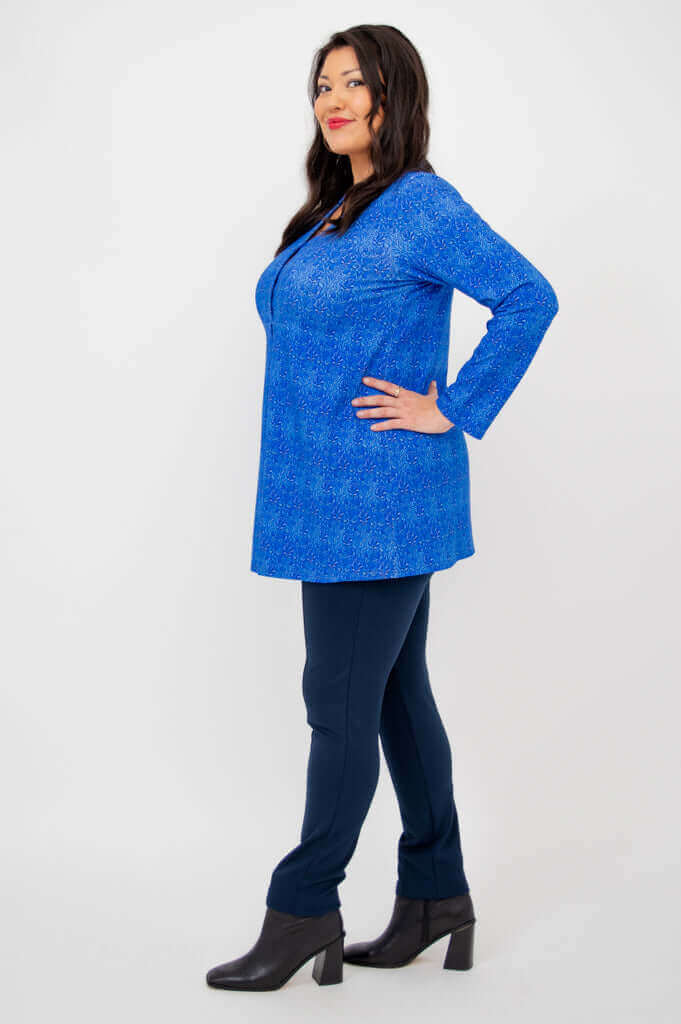Side view of model in a blue V-neck tunic and navy pants, hands on hip
