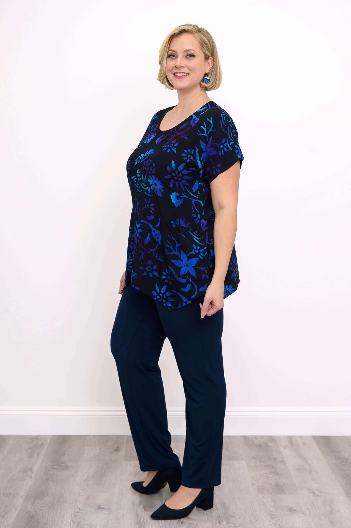 Side view of woman in black floral print curved-hem tunic and navy pants