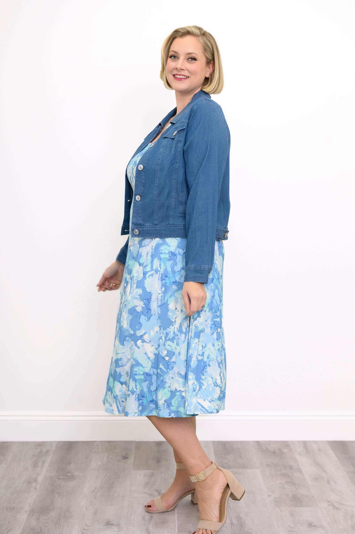 Woman in blue abstract tank dress paired with a denim jacket, side view